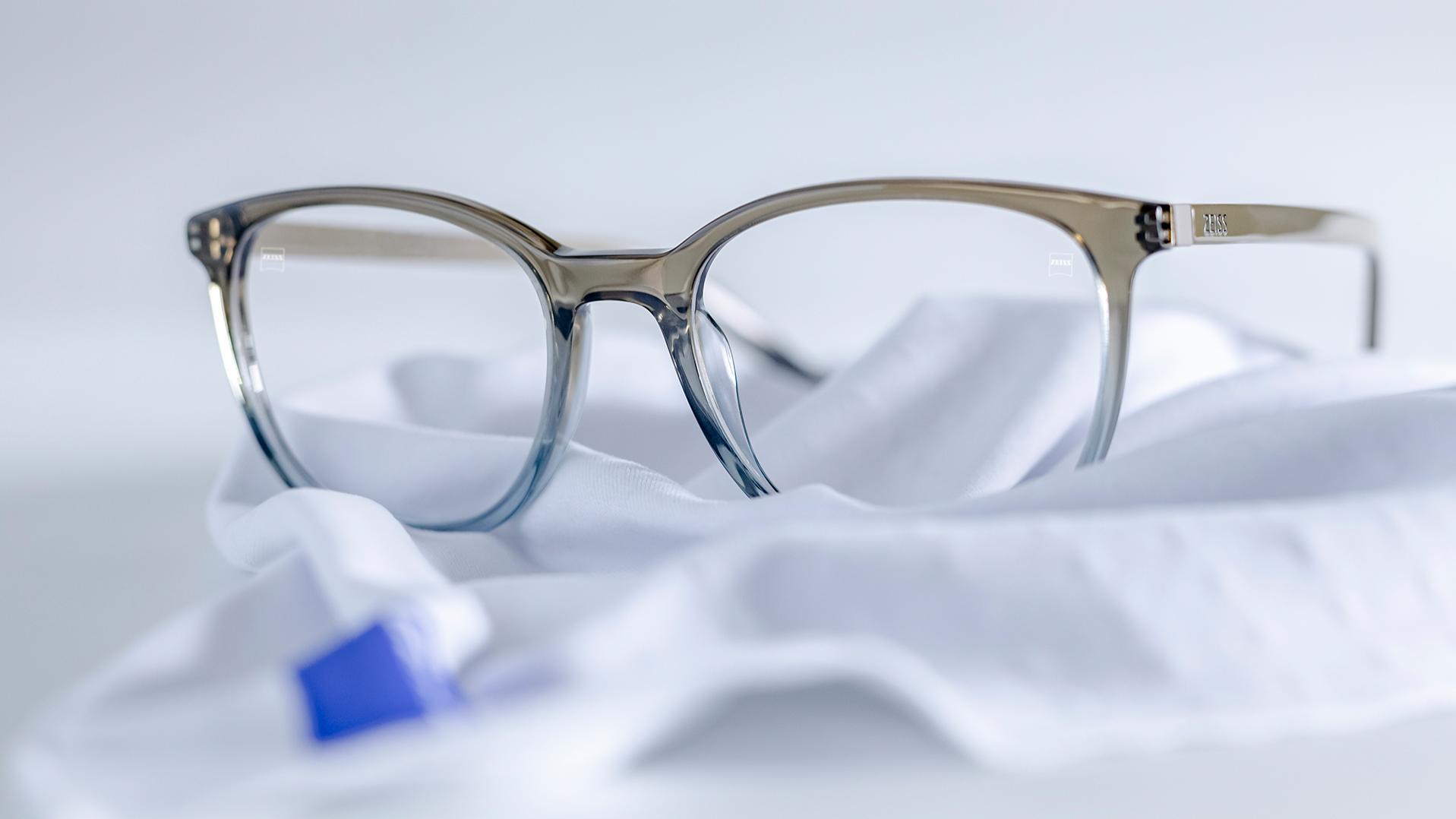 Naočale sa sivo-plavim okvirom i ZEISS lećama s DuraVision® slojem leže na bijeloj krpi od mikrovlakana.