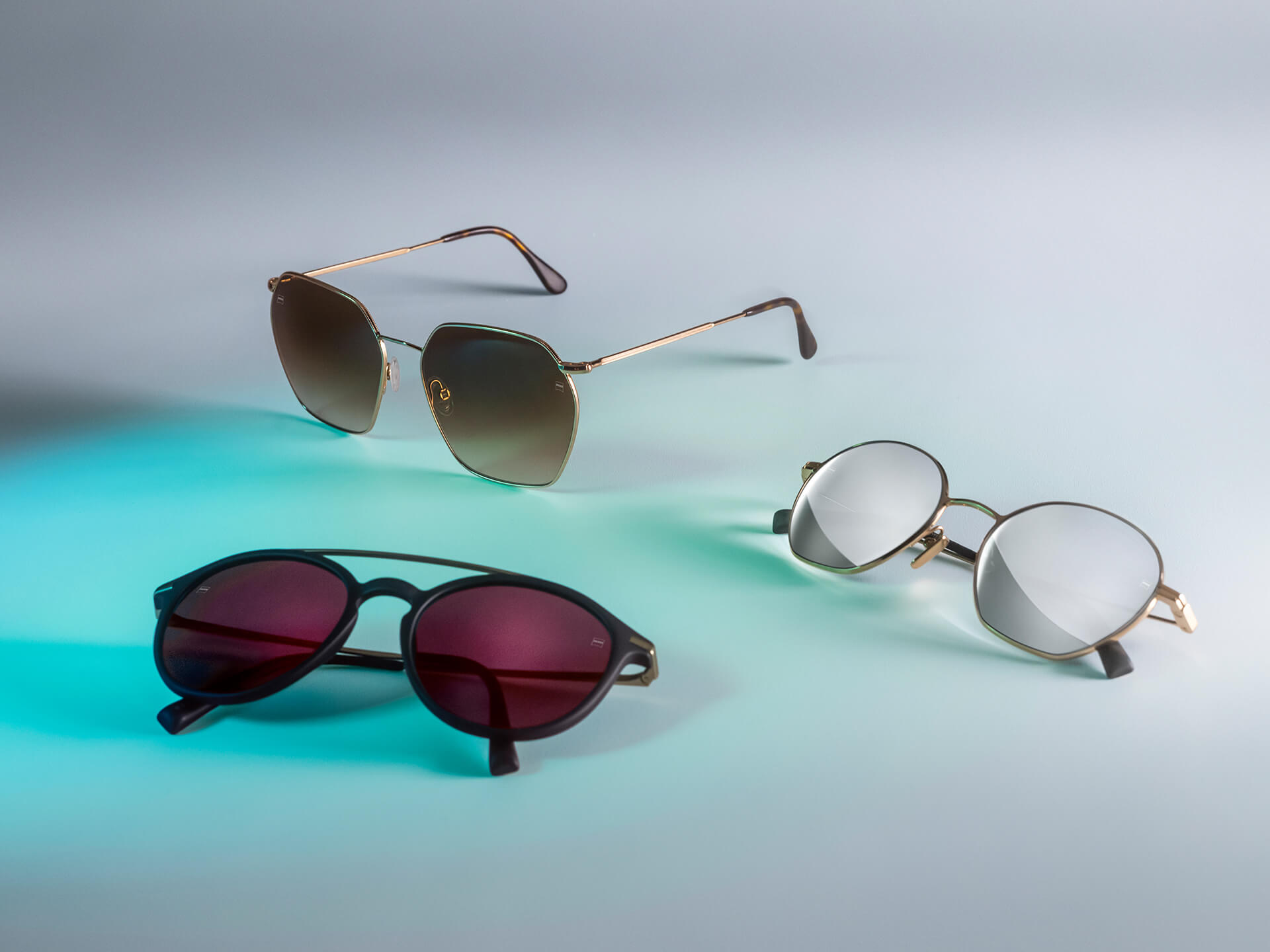 Tri para sunčanih naočala s različitim bojama ZEISS leća za sunčane naočale, s DuraVision Sun, DuraVision Mirror i Flash Mirror slojevima, vidljive na bijeloj pozadini s refleksijom plavog svjetla.