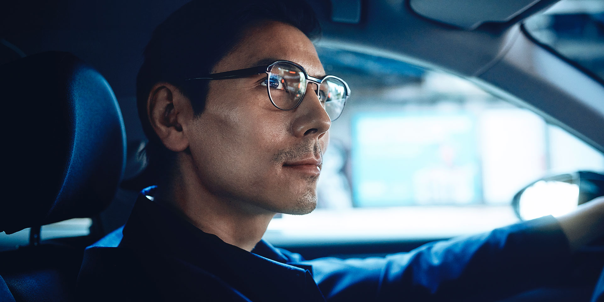 Muškarac vozi automobil, izgleda samopouzdano s blagim osmijehom prema cesti. Nosi ZEISS DriveSafe jednojakosne leće.