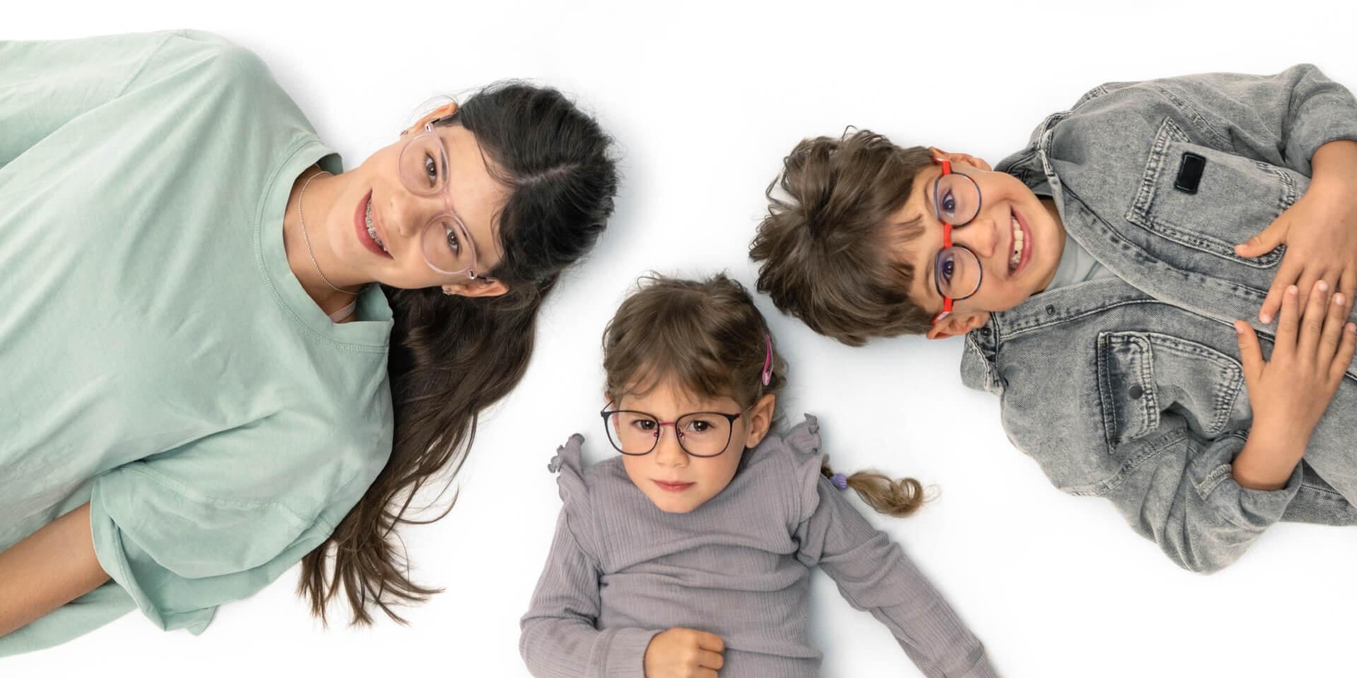 Tinejdžer i dvoje mlađe djece leže na podu i nose leće ZEISS Myopia.