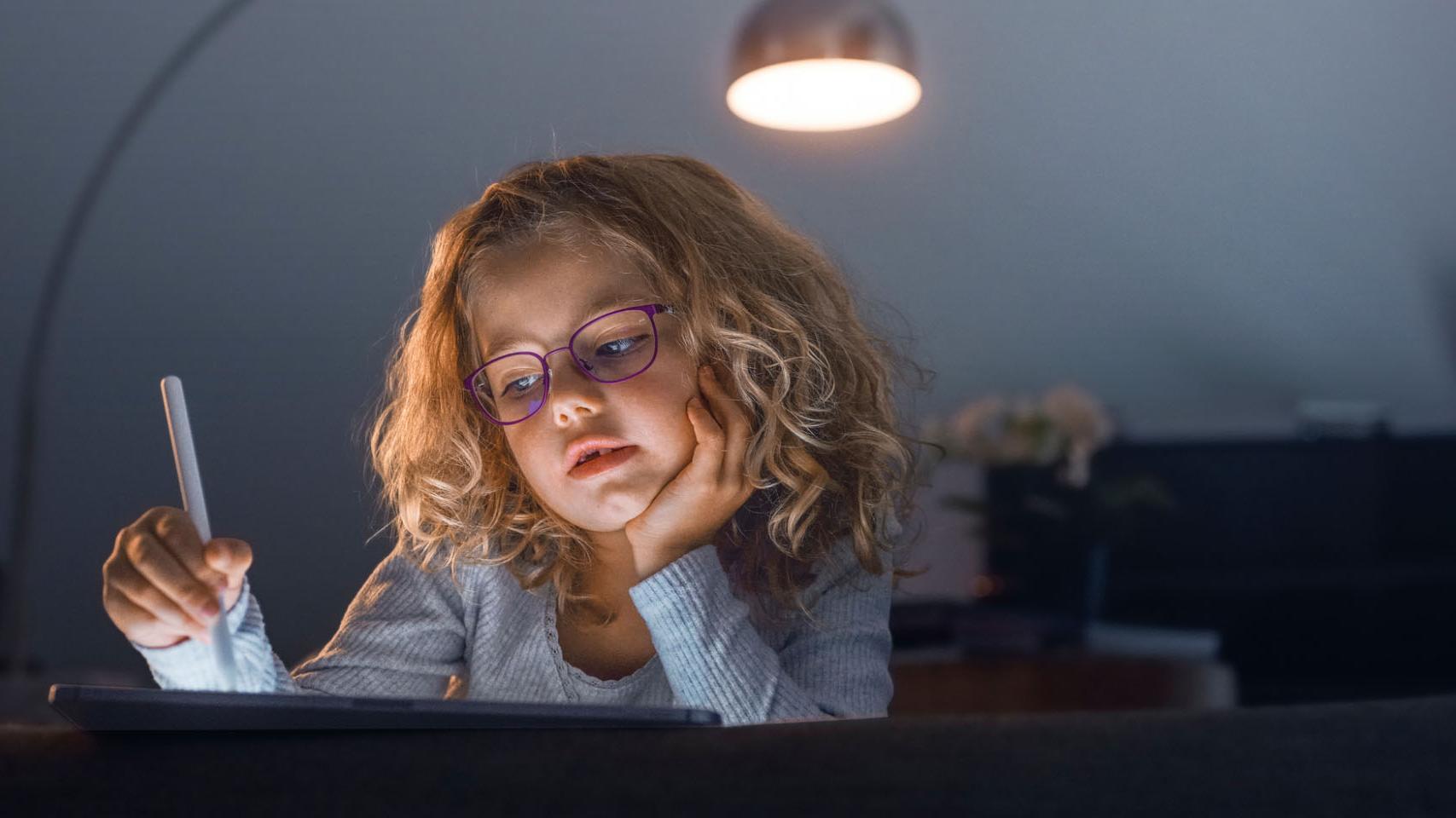 Djevojčica u mračnoj dnevnoj sobi gleda u tablet.