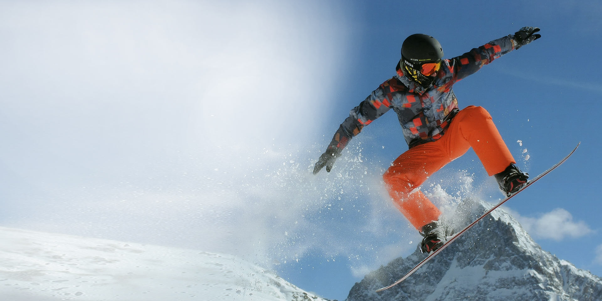 Muškarac skače sa snowboardom, nosi crnu skijašku kacigu i ZEISS naočale za snijeg s tehnologijom Interchargeable za zaštitu