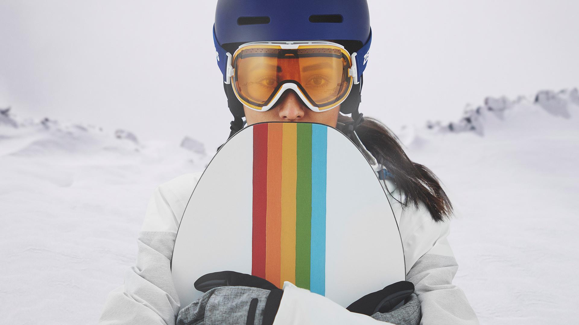 Mlada žena nosi naočale za snijeg sa ZEISS zamjenjivom tehnologijom i drži snowboard.
